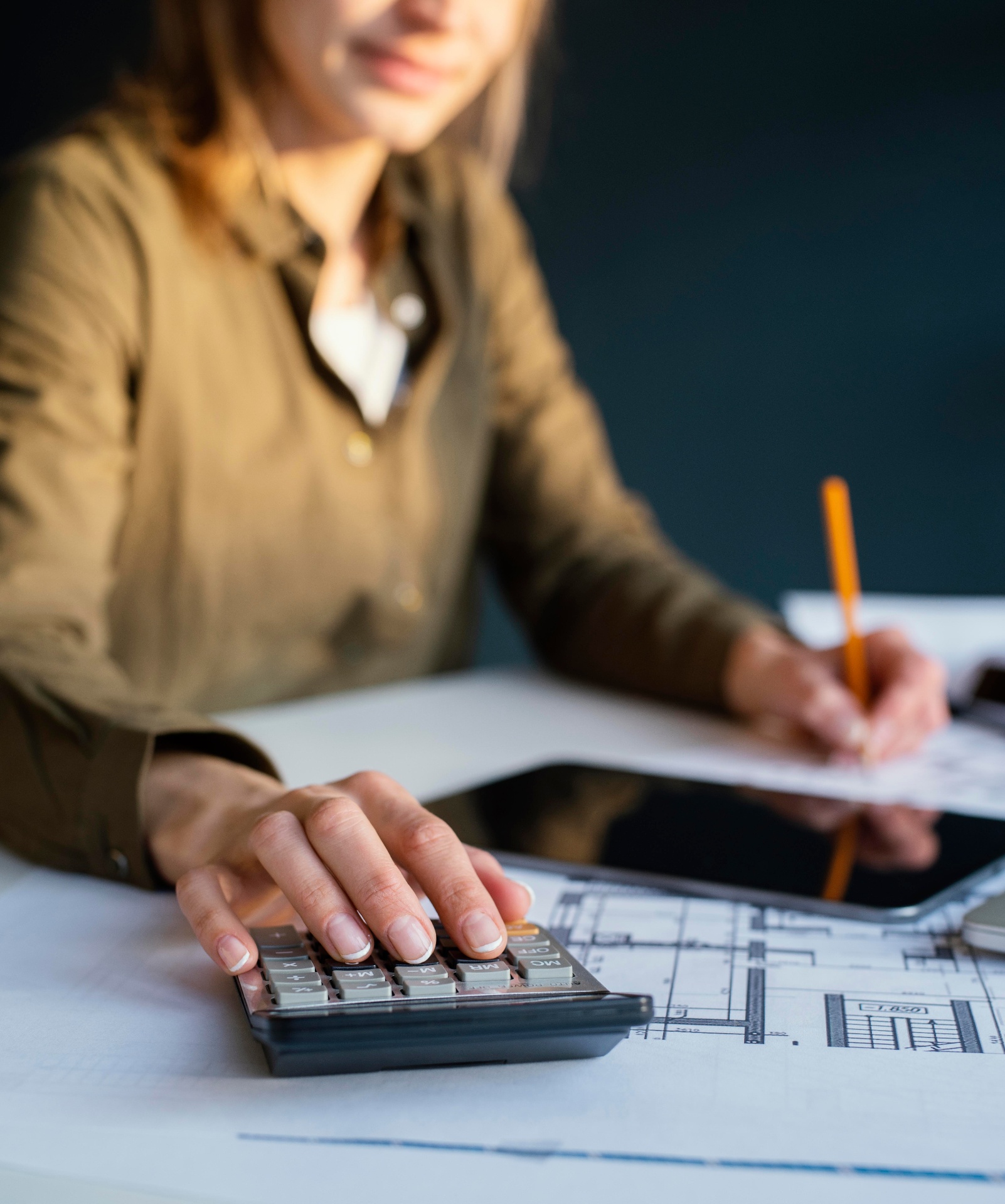 Pessoa anotando planejamento financeiro com calculadora e documentos